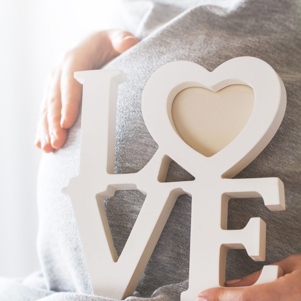 Young pregnant woman holds wooden letters LOVE. Love concept.